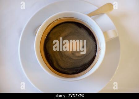 Flat-lay view of an americano, steaming cup of black coffee served in a white porcelain cup, with a small spoon resting on the saucer Stock Photo