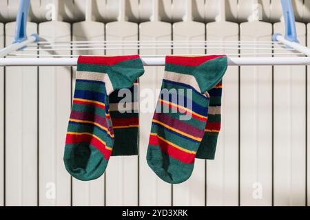 Colorful socks hanging on the clothesline drying on the radiator at home in winter. Stock Photo