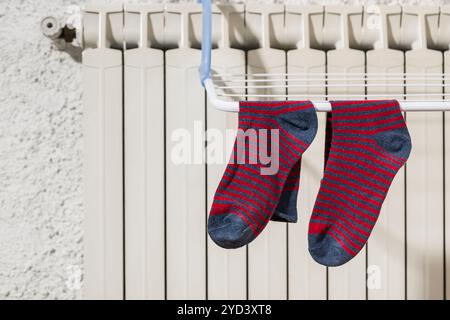 Colorful socks hanging on the clothesline drying on the radiator at home in winter. Stock Photo