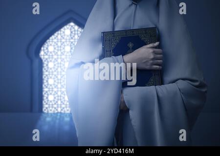 Religious muslim woman with hijab holding holy book of Al Quran in the mosque. Muslim holy book. Concept of Islamic religion, Ramadan kareem, or Eid A Stock Photo