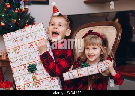 Happy brother and sister in identical Christmas outfits holding gifts Stock Photo