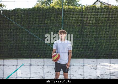 Volleyball player standing on a sand court, holding a ball and preparing for the next play during a quiet moment in an outdoor beach volleyball match. Stock Photo