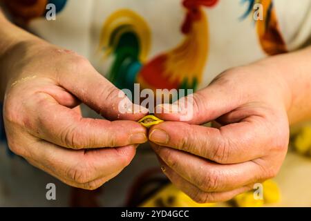 At the Le Sfogline pasta workshop, two hands shape a single tortellino from a filled square of dough. Already-formed tortellini lie ready in the background. Via Belvedere, Bologna, Emilia-Romagna, Italy. Stock Photo