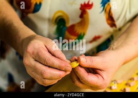 At the Le Sfogline pasta workshop, two hands fold the dough of a tortellino over its filling. Already-finished tortellini lie on the work table in the background. Via Belvedere, Bologna, Emilia-Romagna, Italy. Stock Photo