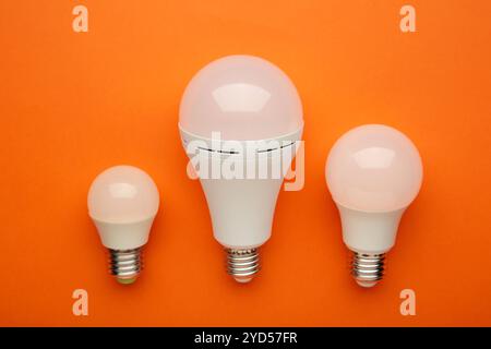 Comparison of different light bulbs on orange background. Top view Stock Photo