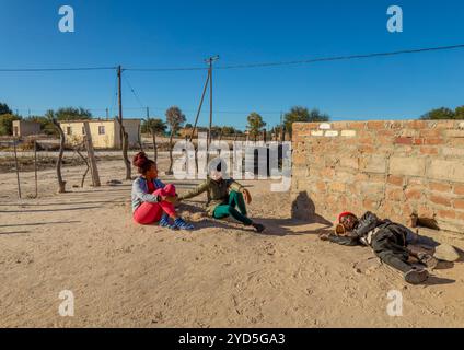 two village African women with braids sited in the yard, drunk man sleeping Stock Photo