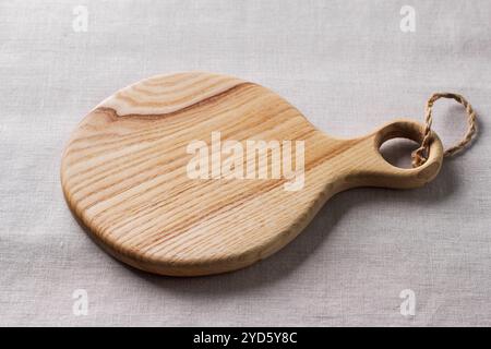 Empty wooden cutting board on a grey woven tablecloth, mockup for creative design. Stock Photo