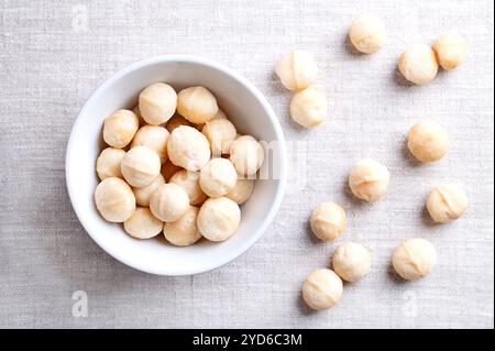 Macadamia nuts, roasted and salted, in a white bowl on linen fabric. Also known as Queensland nut, bush nut, maroochi nut, bauple and Hawaii nuts. Stock Photo