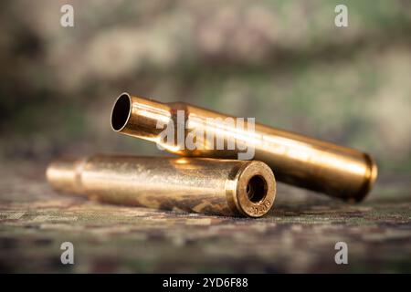 Two rifle bullets cartridges on green military camouflage fabric texture background Stock Photo