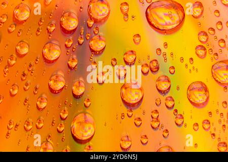 This macro photograph features multiple water droplets of various sizes on a surface with a gradient of colors ranging from yellow to orange and red. Stock Photo