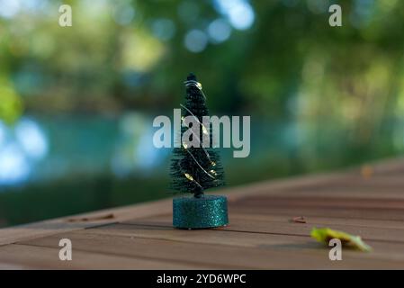 A mini plastic Christmas tree with fairy lights standing on a table in the park with a beautiful bokeh background. Copy space Stock Photo