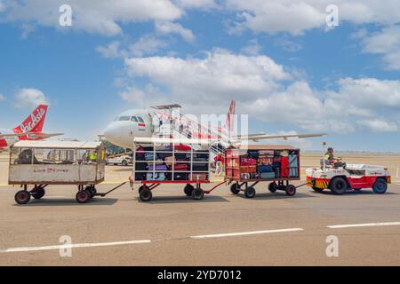 Luggage vehicle cart Baggage Towing Tractor by Lion Group delivering luggage to Airbus A320 of AirAsia,  the terminal before takeoff at Changi Stock Photo