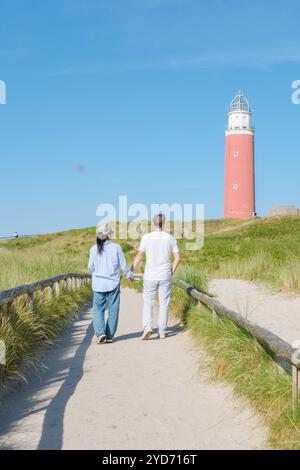 Two individuals strolling along a scenic path near a majestic lighthouse in Texel, Netherlands, surrounded by the calming sounds Stock Photo