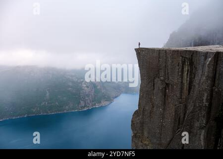 A lone figure stands on the edge of Preikestolen, a dramatic cliff in ...