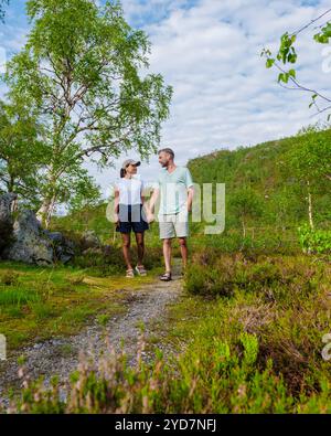 A couple walks hand-in-hand down a path through a lush, green forest in Norway Stock Photo