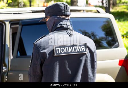 Special Forces police officer in black uniform near a patrol car in summer day. Inscription in russian: Police Stock Photo