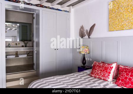 Red embroidered cushions in grey panelled bedroom with view to en suite in historic house on the Island of Tinos in Greece Stock Photo