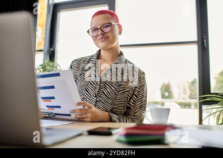A bald woman with pink hair analyzes business reports while seated at her desk Stock Photo