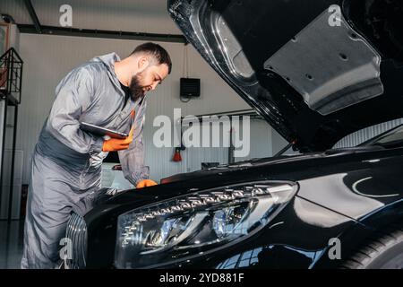 Car mechanic working with a laptop in Auto Repair Service checking car engine Stock Photo
