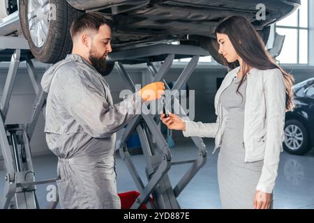 Auto Mechanic giving the car keys to his female customer in workshop at auto repair center. Quality of Service Stock Photo