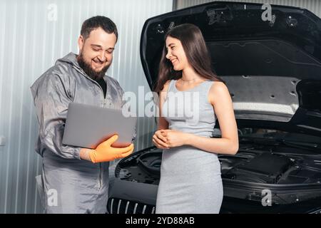 Car mechanic communicating with a female customer while using laptop and examining vehicle breakdown at auto repair shop Stock Photo