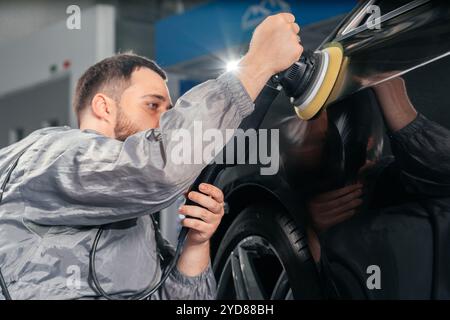 Worker polishing car with special grinder and wax from scratches at the car service station. Professional car detailing and main Stock Photo