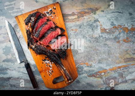 Traditional barbecue dry aged Kobe tomahawk steak with salt served as top view on a wooden design board with a Japanese Satoku k Stock Photo