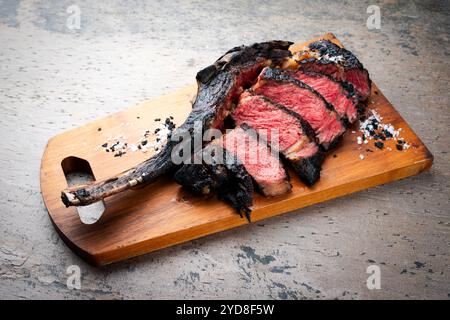 Traditional barbecue dry aged Kobe tomahawk steak with salt and black salt crystals served as close-up on a wooden design board Stock Photo