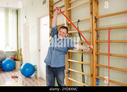 A young man with Down syndrome is stretching with a red pole in a gymnasium. He is smiling and looks happy. Stock Photo