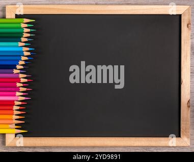 Sharp colored pencils are arranged in an orderly manner on a black board with copy space. Close-up: school - stationery. Stock Photo