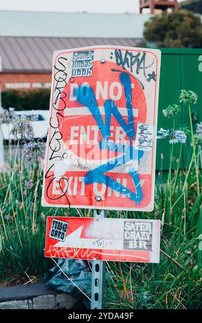 A dirty, graffitied street sign in Los Angeles covered in stickers. It says 'Do Not Enter' on one line and below that 'Exit Only.' Stock Photo