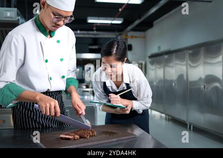 Student cooking apprentice Take notes on every step as the chef cooks in the culinary academy's kitchen. Stock Photo