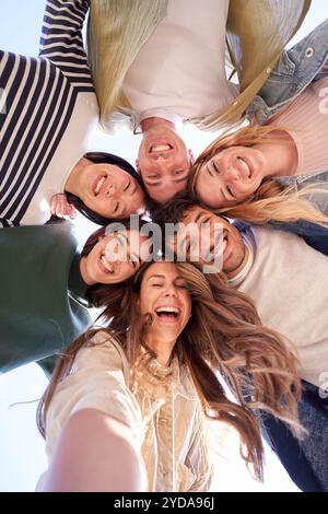 Selfie portrait from below of diverse gen z group friends posing smiling in circle looking at camera Stock Photo