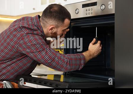 Repairman with screwdriver fixing oven in kitchen Stock Photo
