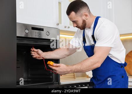 Repairman testing oven element with multimeter in kitchen Stock Photo