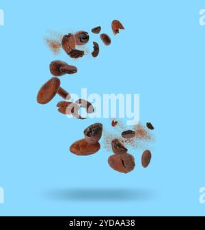 Cocoa beans and powder in air on light blue background Stock Photo