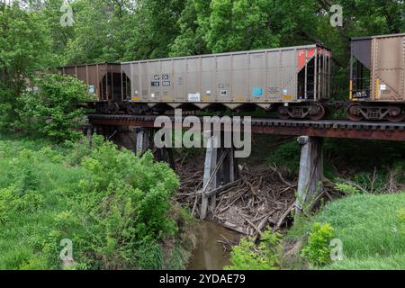 Railroad cars on wooden trestle in Cloud County, Kansas. Steam running underneath the bridge. Green grass in foreground, trees in background. Stock Photo