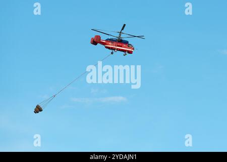 Big fire rescue red colour helicopter gets water tank for damping fire bright blue sky day Stock Photo