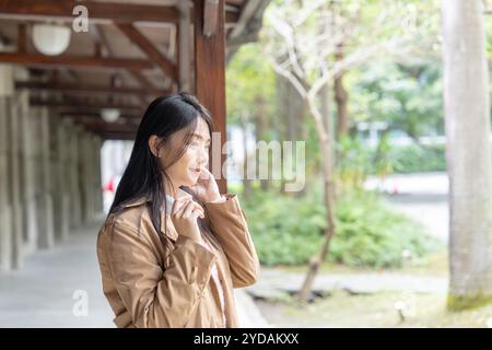 A long-haired Taiwanese woman in her 20s wearing a beige trench coat spends her winter afternoon under the eaves in Xinyi District, Taipei, Taiwan, on Stock Photo