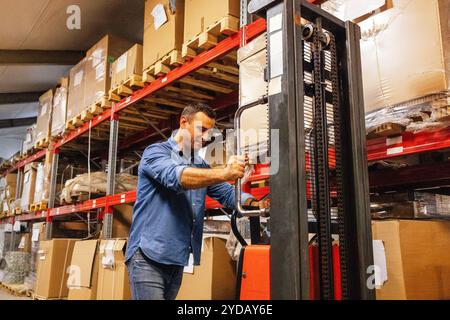 A young smiling man in a warehouse with a forklift truck. An attractive worker in casual clothes Stock Photo