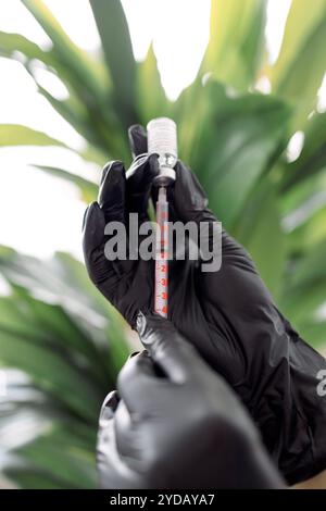 A woman hands in black gloves holding a syringe and a vial of serum. The cosmetologist fills a syringe with a moisturizing essen Stock Photo