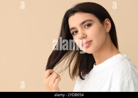 Young woman with dandruff problem examining her hair on beige background Stock Photo