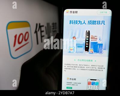 In this photo illustration, a person is holding a cellphone with the webpage of Chinese online education platform company Zuoyebang in front of logo. Stock Photo