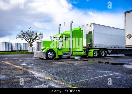 Industrial classic bonnet big rig bright green semi truck with extended cab for truck driver rest and dry van semi trailer standing on the truck stop Stock Photo