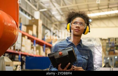 A young female worker is controlling a mechanical robot. to sort out the items that come into the warehouse to wait for the next Stock Photo