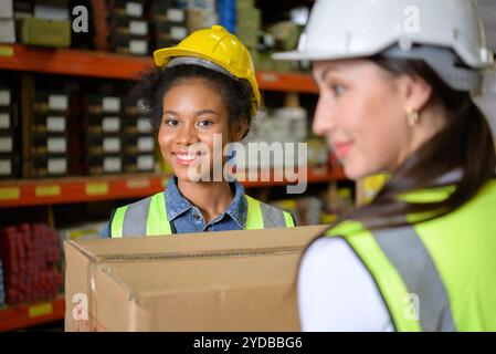 Two girls warehouse workers Help each other lift heavy boxes to move storage. Stock Photo