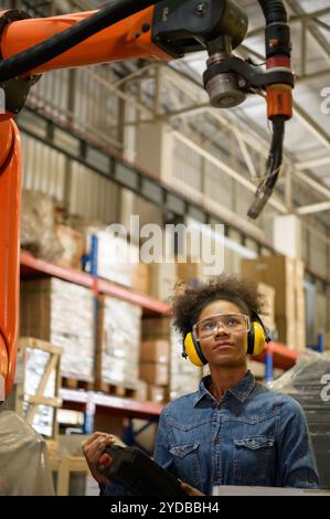 A young female worker is controlling a mechanical robot. to sort out the items that come into the warehouse to wait for the next Stock Photo