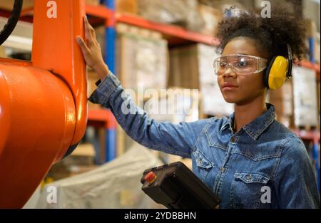 A young female worker is controlling a mechanical robot. to sort out the items that come into the warehouse to wait for the next Stock Photo