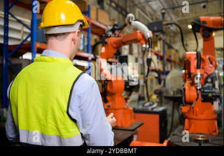 A male worker is controlling a welding robot. by using forcing welding with a control screen which is used for precision welding Stock Photo