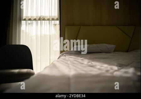 A bedroom showing the golden morning sun shining through the curtains through the window into the room Stock Photo
